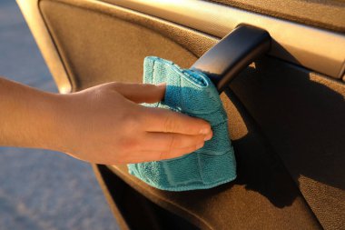 Man with duster sanitizing car door handle outdoors, closeup