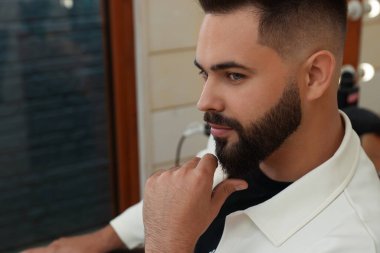 Young man with fresh haircut and groomed beard in barbershop