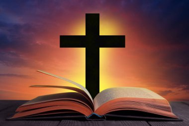 Silhouette of cross and open Bible on wooden table at sunset