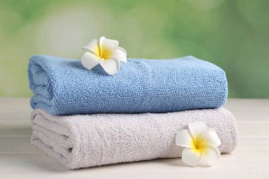 Soft folded towels and plumeria flowers on white wooden table