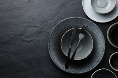 Set of clean tableware on black table, flat lay. Space for text