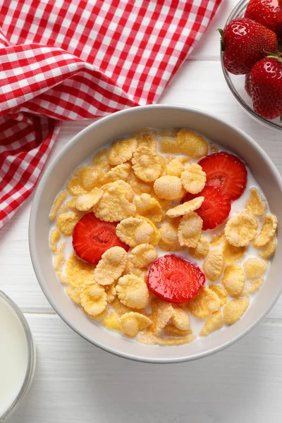 Corn flakes with strawberries in bowl served on white wooden table, flat lay