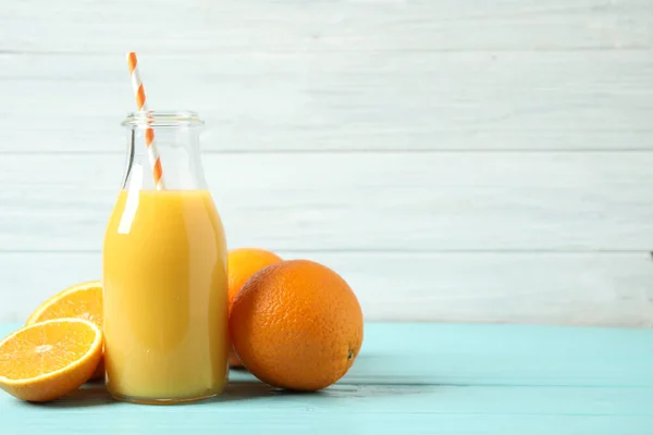 Bottle of orange juice and fresh fruits on light blue wooden table. Space for text