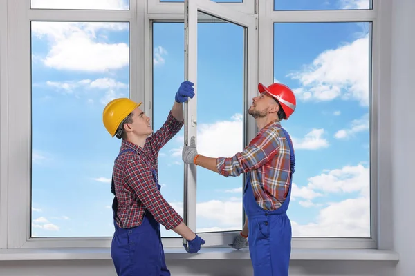 Workers in uniform installing plastic window indoors