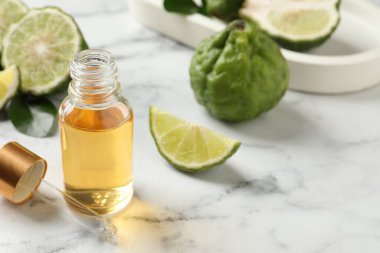 Bottle of essential oil, pipette and fresh bergamot fruits on white marble table. Space for text