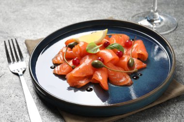 Salmon carpaccio with capers, cranberries, basil and lemon served on grey table