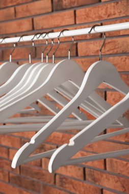 White clothes hangers on rail near red brick wall, closeup