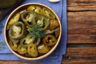 Bowl with slices of pickled green jalapeno peppers on wooden table, top view. Space for text