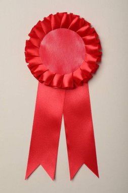 Red award ribbon on beige background, top view
