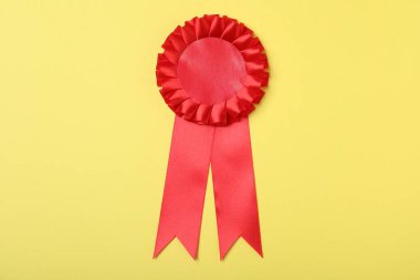 Red award ribbon on yellow background, top view