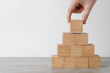 Woman building pyramid with wooden cubes at table, closeup and space for text. Management concept