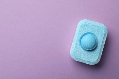 Water softener tablet on violet background, top view. Space for text
