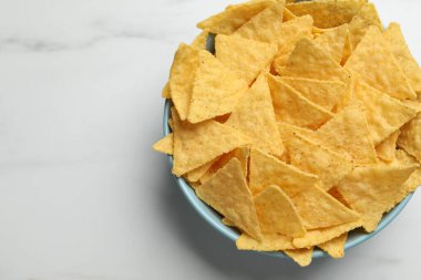 Tortilla chips (nachos) in bowl on white table, top view. Space for text