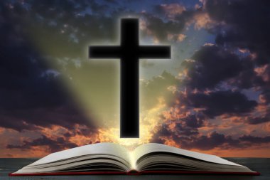 Silhouette of cross and open Bible on table against cloudy sky