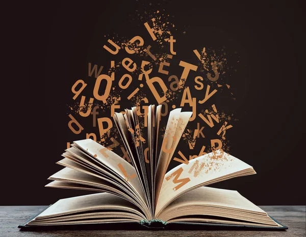 Open book with flying letters on wooden table against brown background. Dyslexia concept