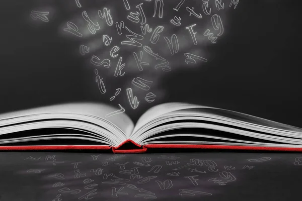 Open book with flying letters on black background. Dyslexia concept