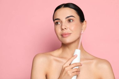 Pembe arka planda yüksek frekanslı darsonval cihaz kullanan bir kadın. Metin için boşluk