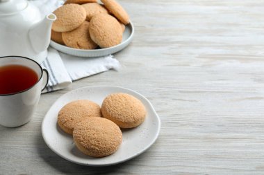 Delicious sugar cookies and cup of tea on white wooden table, space for text