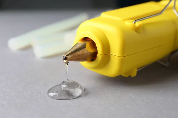 Melted glue dripping out of hot gun nozzle on grey background, closeup