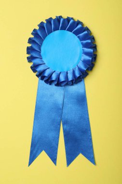 Blue award ribbon on yellow background, top view