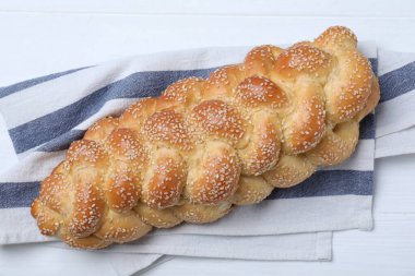 Homemade braided bread with sesame seeds on white wooden table, top view. Traditional challah