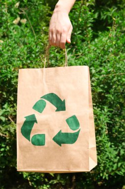 Woman holding paper bag with recycling symbol outdoors, closeup