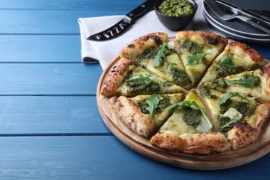 Delicious pizza with pesto, cheese and arugula on blue wooden table. Space for text