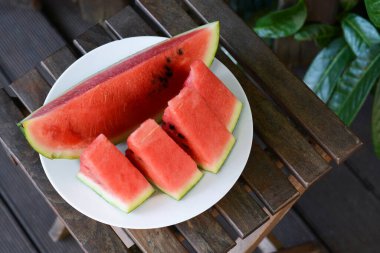 White plate with sliced watermelon on wooden stool outdoors. Space for text