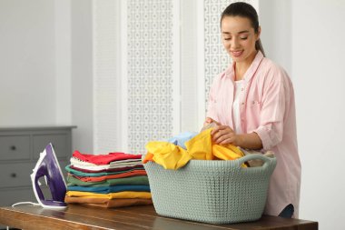 Young woman with basket full of clean laundry at wooden table indoors