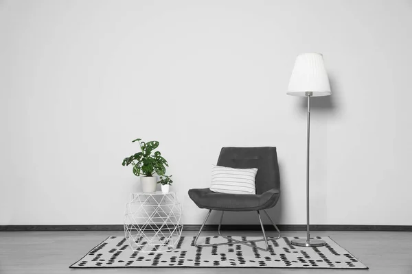Stylish armchair, floor lamp and plants near white wall
