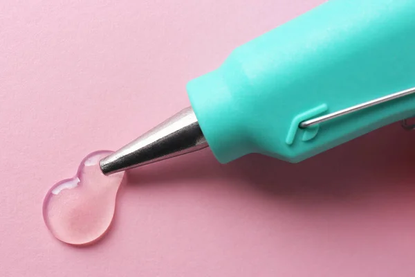 Melted glue dripping out of hot gun nozzle on pink background, closeup