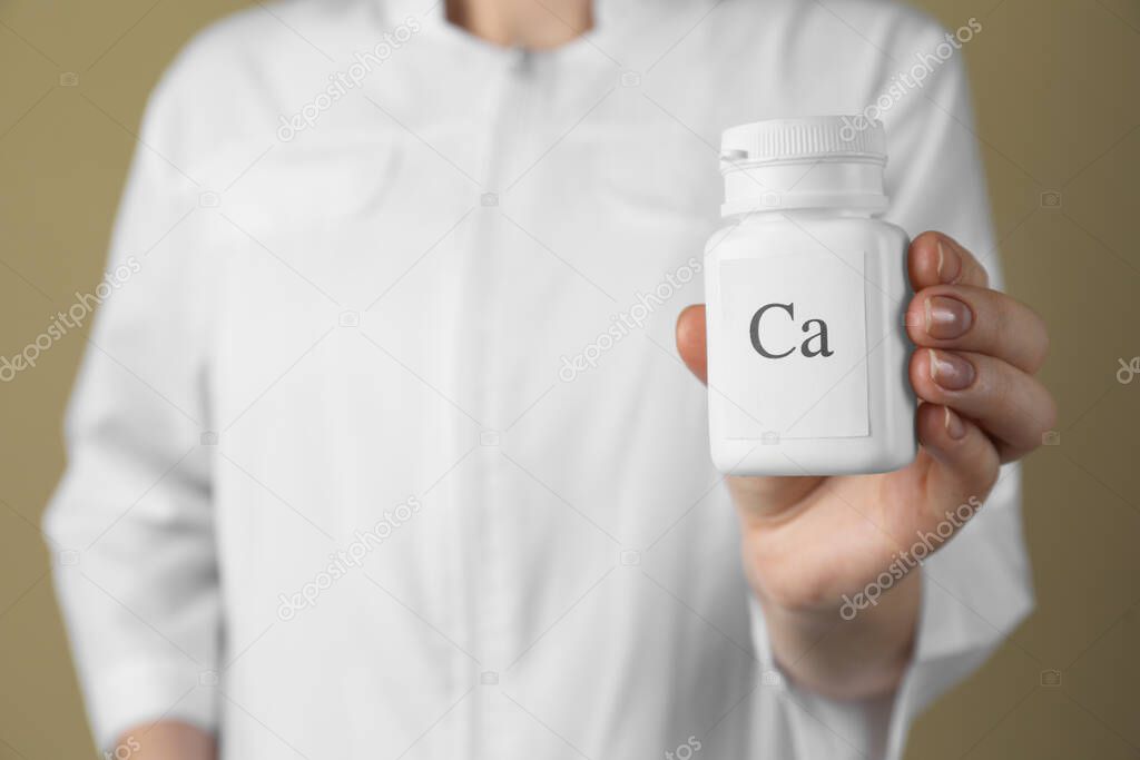 Calcium supplement. Doctor holding bottle with pills on beige background, closeup