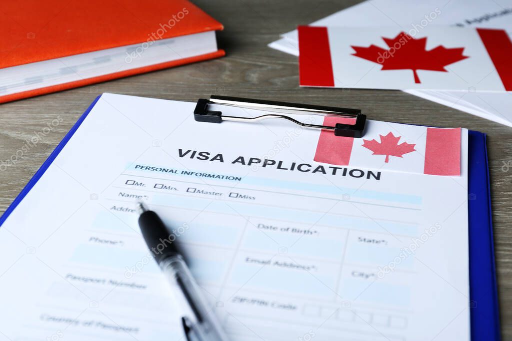 Visa application form for immigration to Canada and pen on wooden table, closeup