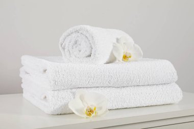 Clean soft white towels with flowers on table against light grey background