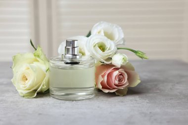 Bottle of perfume and flowers on grey table indoors