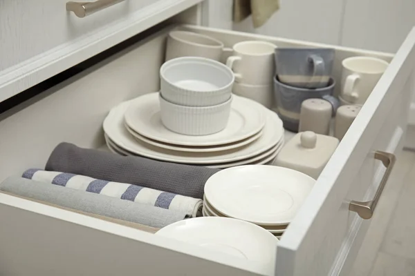 Open drawer of kitchen cabinet with different dishware and towels, closeup