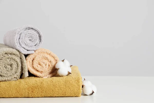 Clean soft towels with cotton flowers on white table against light grey background. Space for text