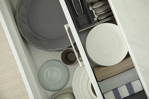 Open drawers of kitchen cabinet with different dishware and towels, top view