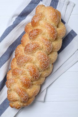 Homemade braided bread with sesame seeds on white wooden table, top view. Traditional challah