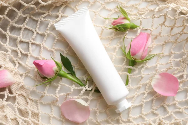 Tube of hand cream and roses in net bag on table, flat lay