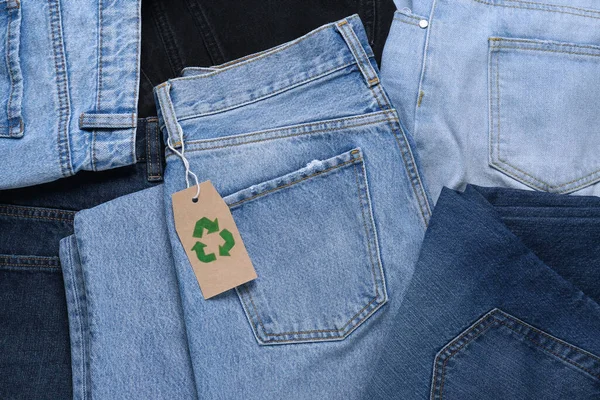 Different jeans with recycling label as background, top view
