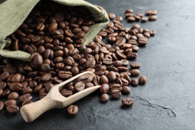 Bag and wooden scoop with roasted coffee beans on black table, closeup. Space for text