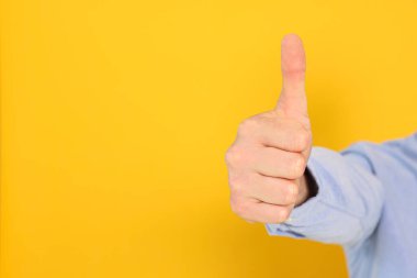 Man showing thumb up on orange background, closeup. Space for text