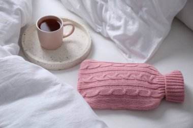 Sıcak su şişesi örgü örülmüş ve yatağın üzerinde bir fincan çay