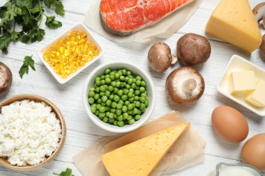 Beyaz ahşap masa üzerinde D vitamini açısından zengin ürünlerin olduğu düz bir kompozisyon.