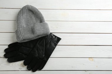 Stylish black leather gloves and hat on white wooden background, flat lay. Space for text