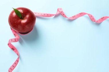 Fresh red apple with measuring tape on light blue background, flat lay. Space for text