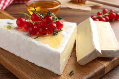 Brie cheese served with red currants and honey on wooden table, closeup