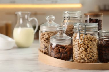 Glass containers with different breakfast cereals on white marble table in kitchen. Space for text