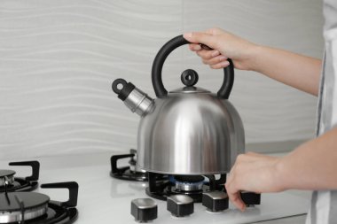 Woman putting kettle on gas stove in kitchen, closeup